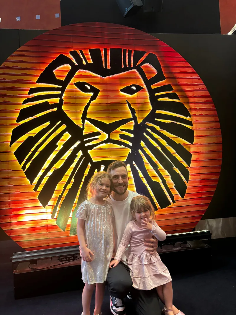 Andy Crebar with his two daughters in front of The Lion King sign