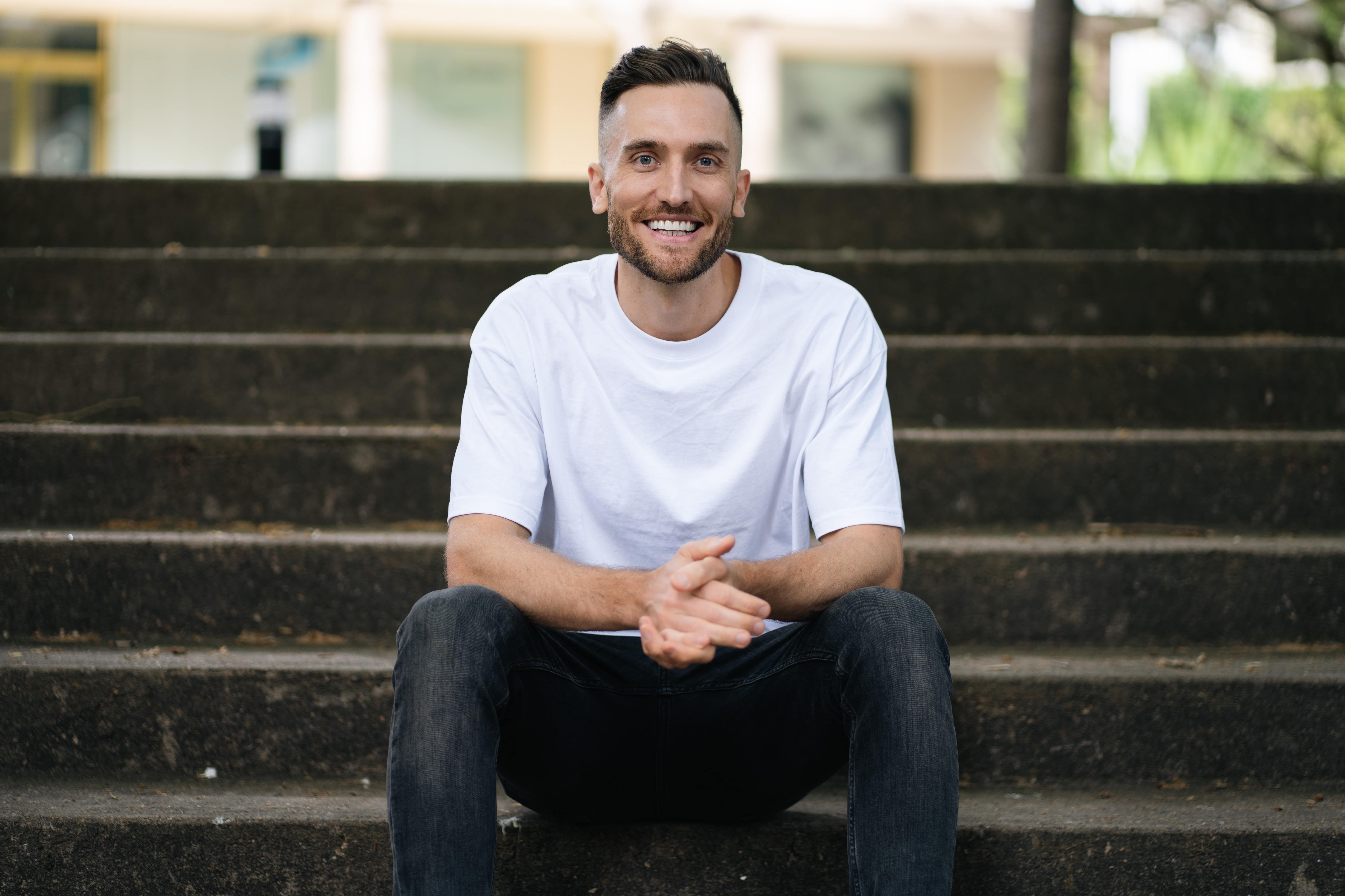 Andy Crebar sitting on concrete steps wearing a plain white t-shirt